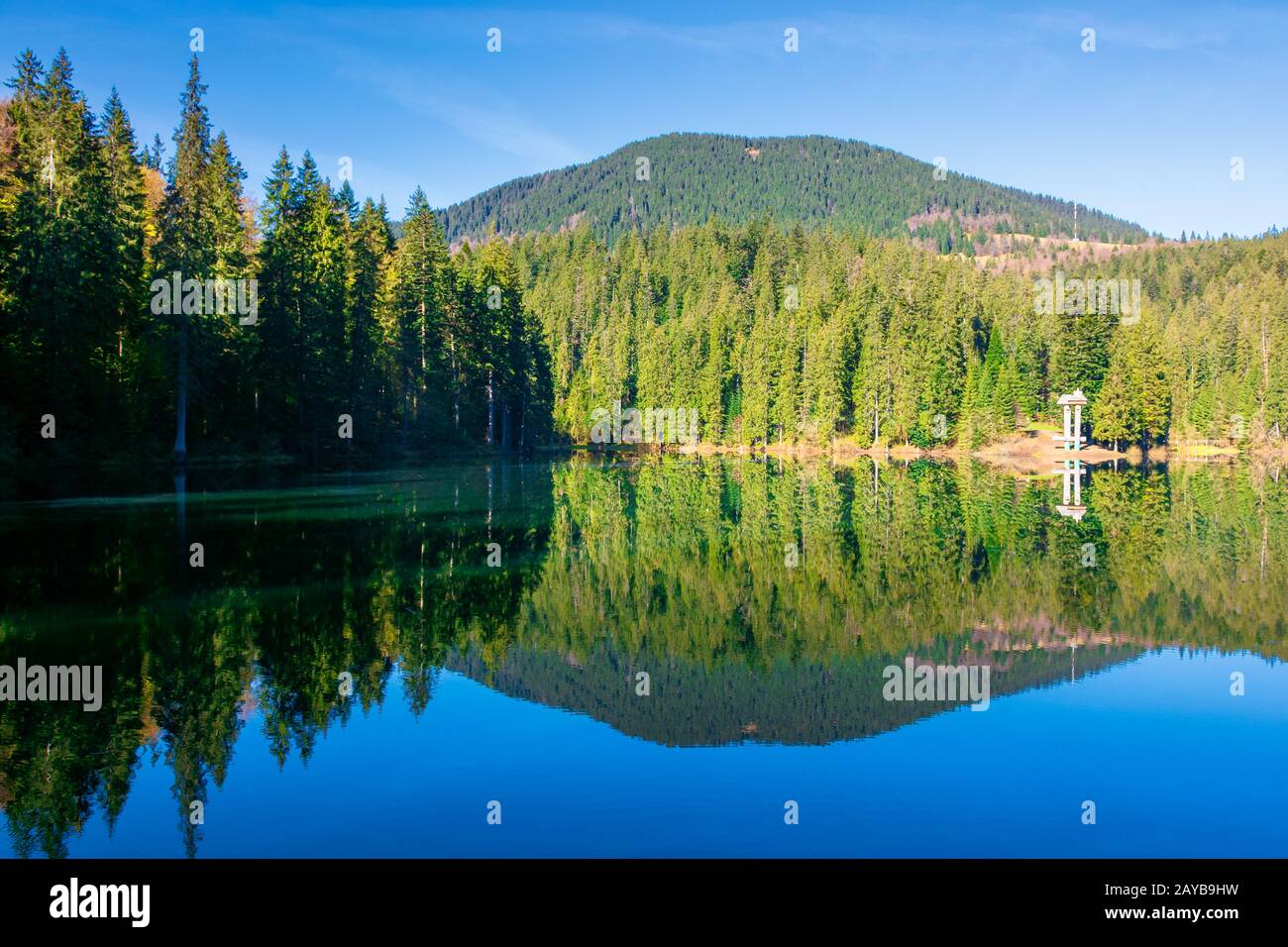 lago di montagna tra la foresta di conifere. natura del mattino scenario con riflessi in acqua calma. tempo soleggiato con cielo blu nuvoloso in primavera. Foto Stock
