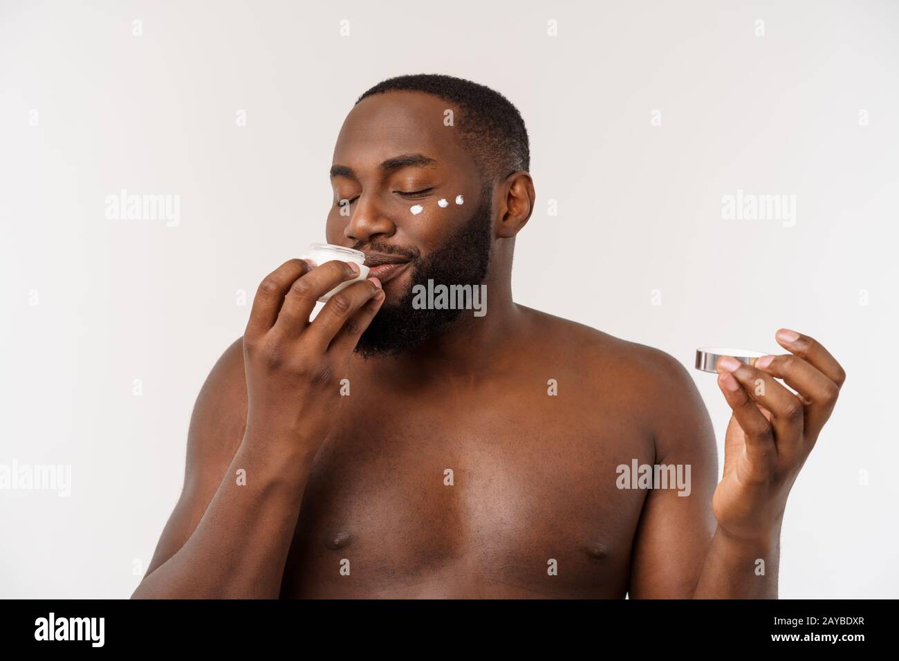Sorridente uomo afro applicare la crema sul suo volto. L'uomo la cute del concetto di cura Foto Stock
