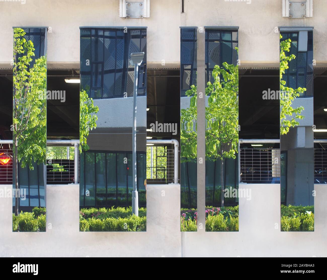 una strada urbana con un moderno edificio di uffici e alberi riflessi in superfici speculari su una struttura di parcheggio auto Foto Stock