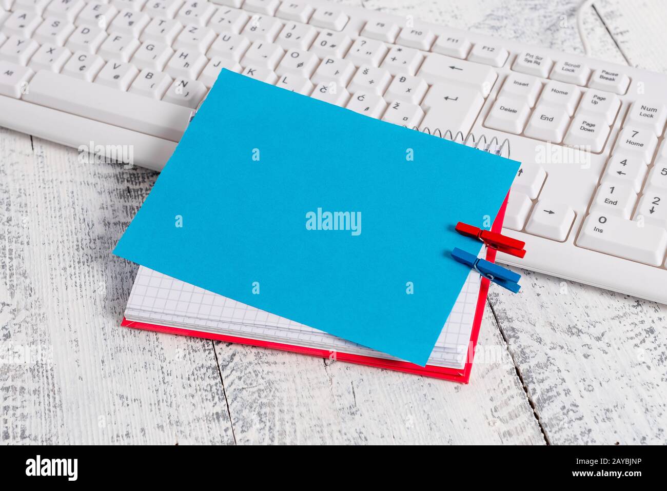 Quaderno di carta quadrato con una nota vuota a forma di rettangolo sopra fissata da due zoccoli sul foglio. Tastiera bianca sotto una c Foto Stock