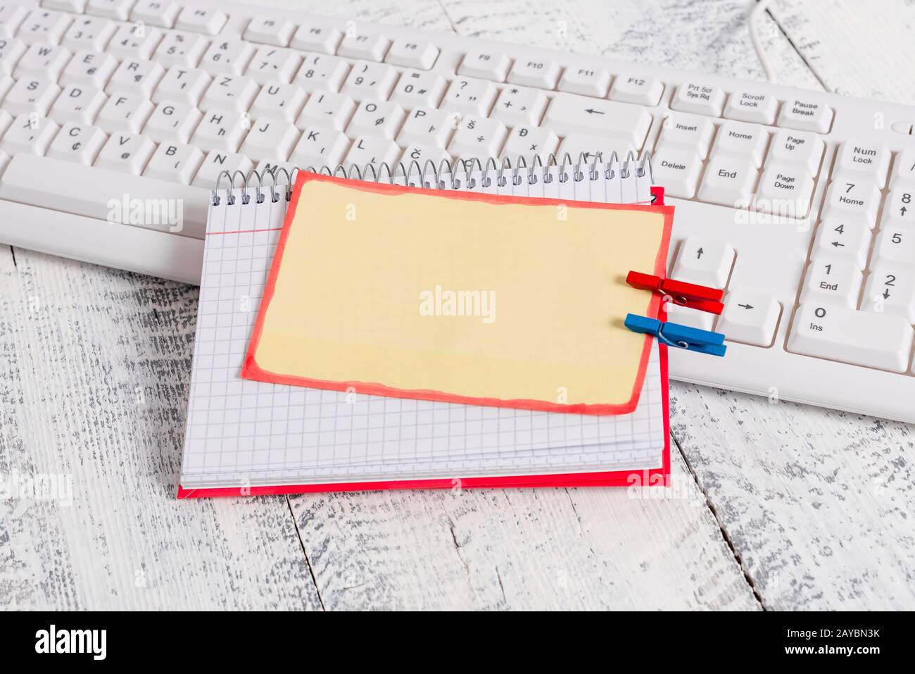 Quaderno di carta quadrato con una nota vuota a forma di rettangolo sopra fissata da due zoccoli sul foglio. Tastiera bianca sotto una c Foto Stock