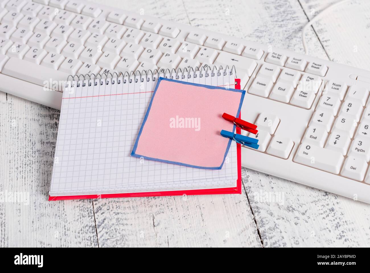 Quaderno di carta quadrato con una nota vuota a forma di rettangolo sopra fissata da due zoccoli sul foglio. Tastiera bianca sotto una c Foto Stock