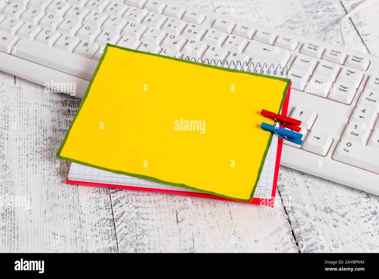 Quaderno di carta quadrato con una nota vuota a forma di rettangolo sopra fissata da due zoccoli sul foglio. Tastiera bianca sotto una c Foto Stock