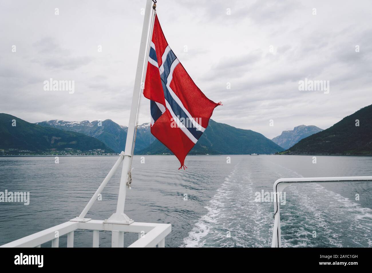 Bandiera norvegese appesa sulla ringhiera della nave e sventola sopra l'acqua. Fiordo norvegano con bandiera. Viaggio in traghetto in Norvegia. Foto Stock