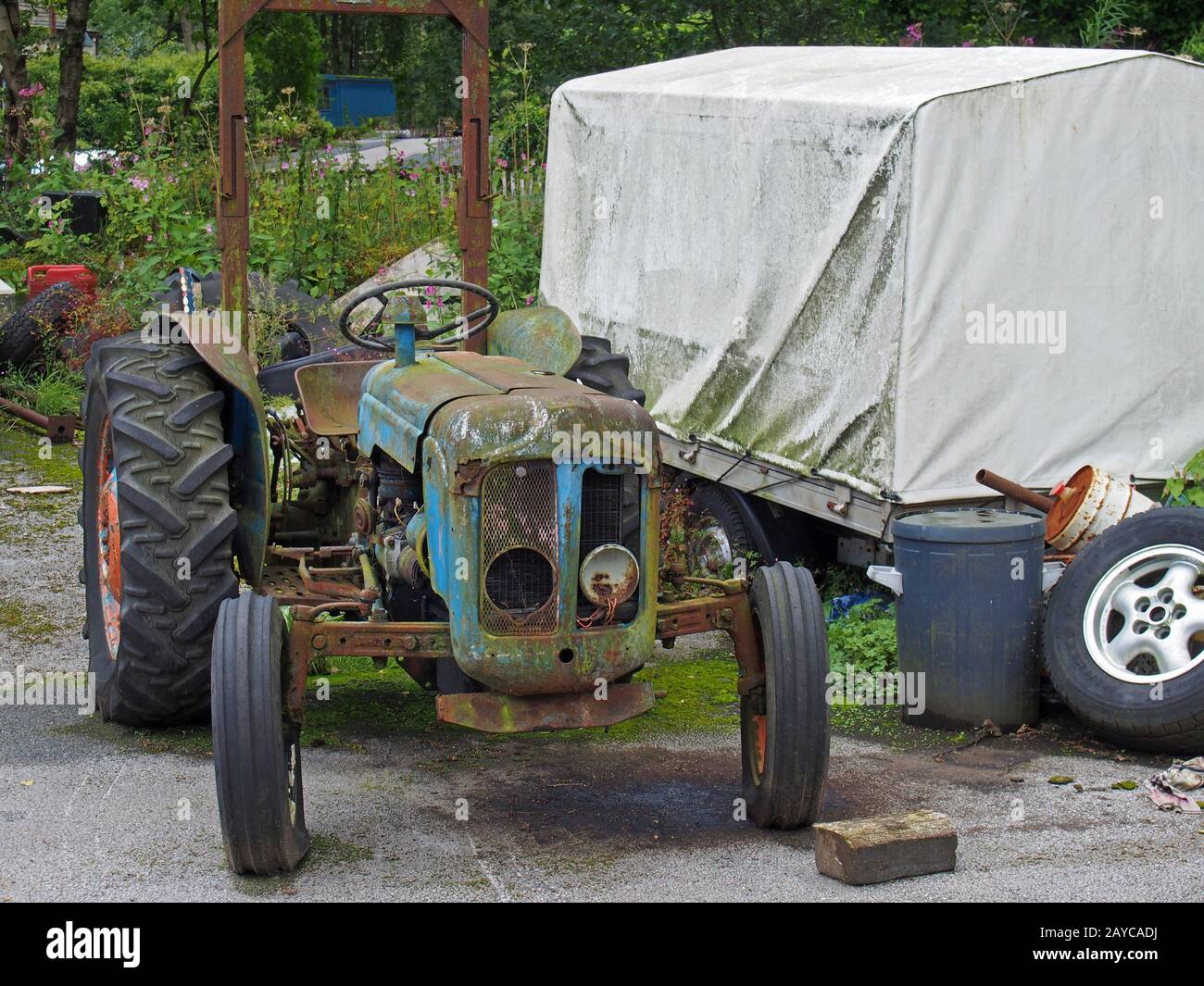 un vecchio trattore abbandonato arrugginendo vicino ad un rimorchio coperto e spazzatura sporchi del telone in un cortile Foto Stock