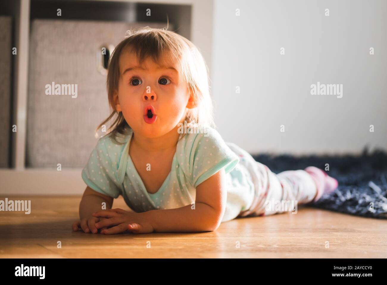 Adorabile bambina sdraiato sul tappeto con espressione divertente Foto Stock