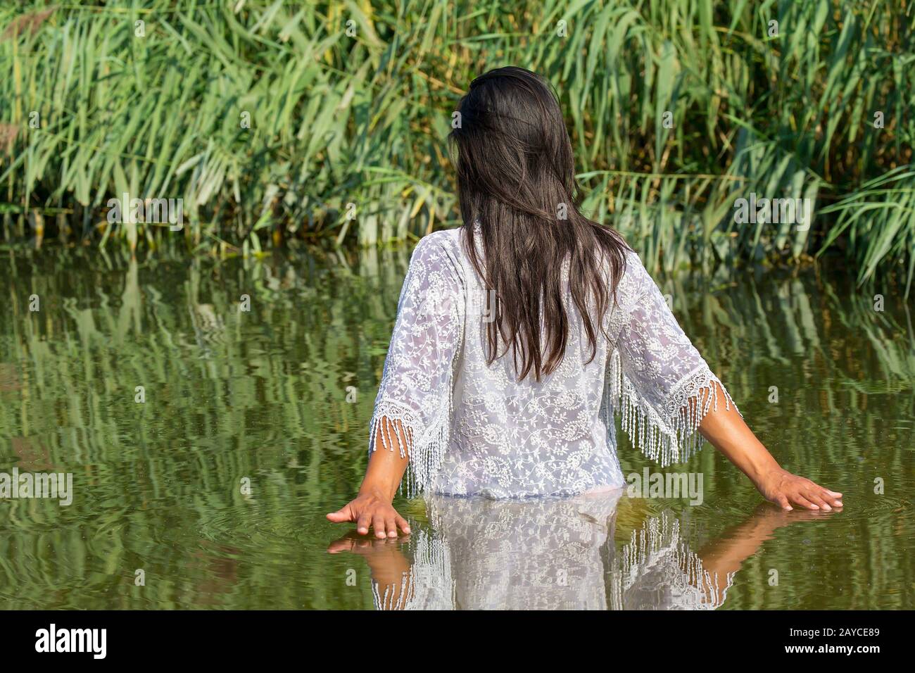 Donna cammina in acqua naturale vicino alle piante di canna Foto Stock