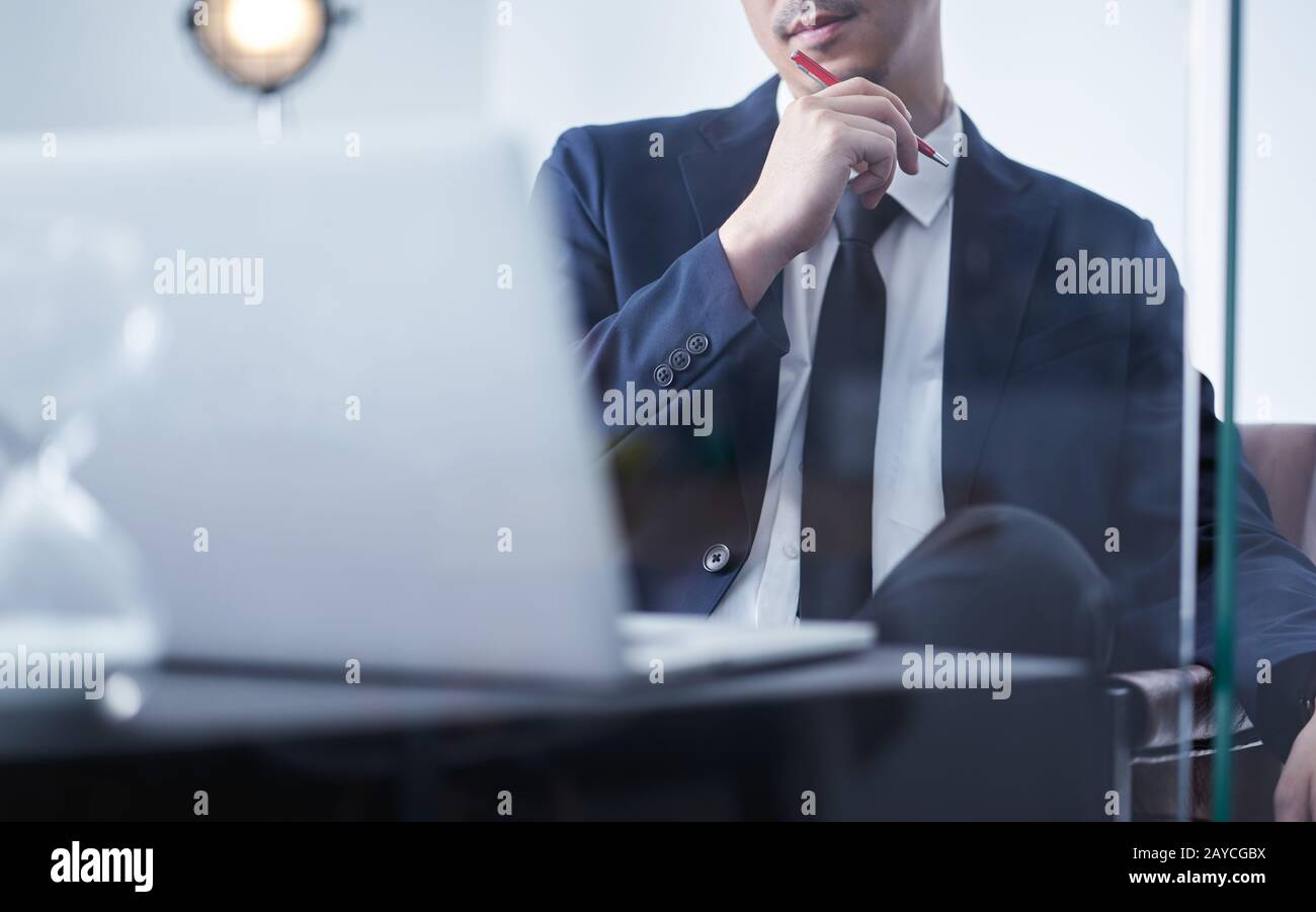 Giovane uomo d’affari asiatico che tiene la penna e pensa al piano finanziario Foto Stock