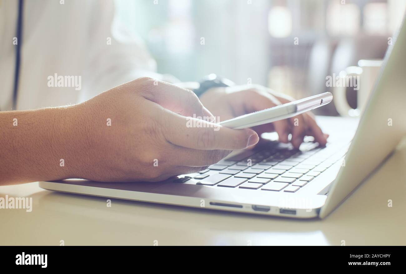 l'uomo d'affari utilizza lo smartphone e codifica i dati sul laptop Foto Stock