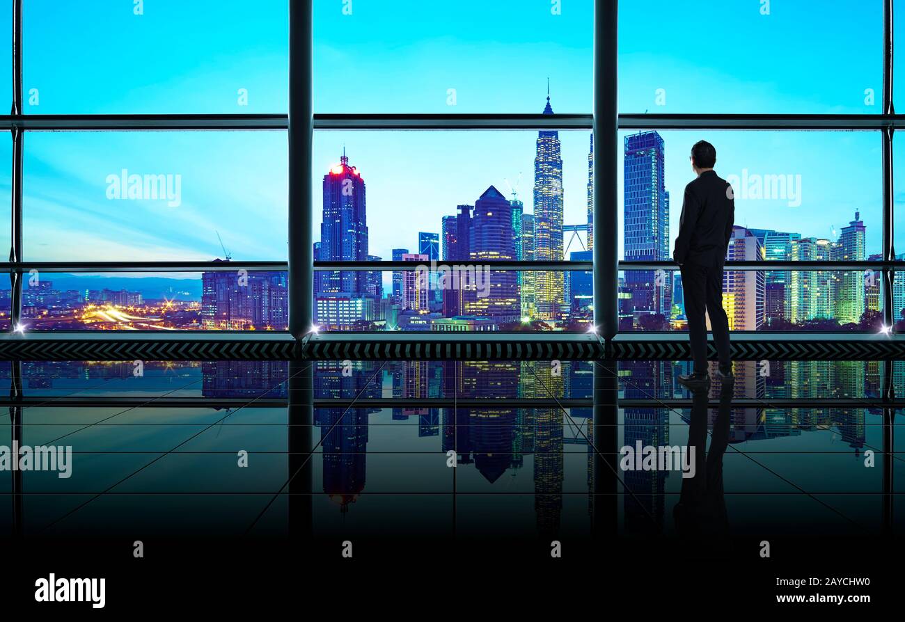 Vista sul retro di un pensieroso uomo d'affari che guarda attraverso la finestra alla grande città moderna Foto Stock