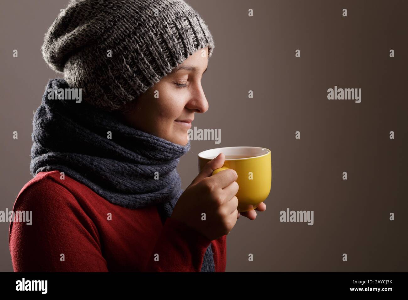 Giovane donna che indossa una sciarpa di lana e un cappuccio di bere il tè caldo. In autunno e inverno e concetto di malattia. Foto Stock