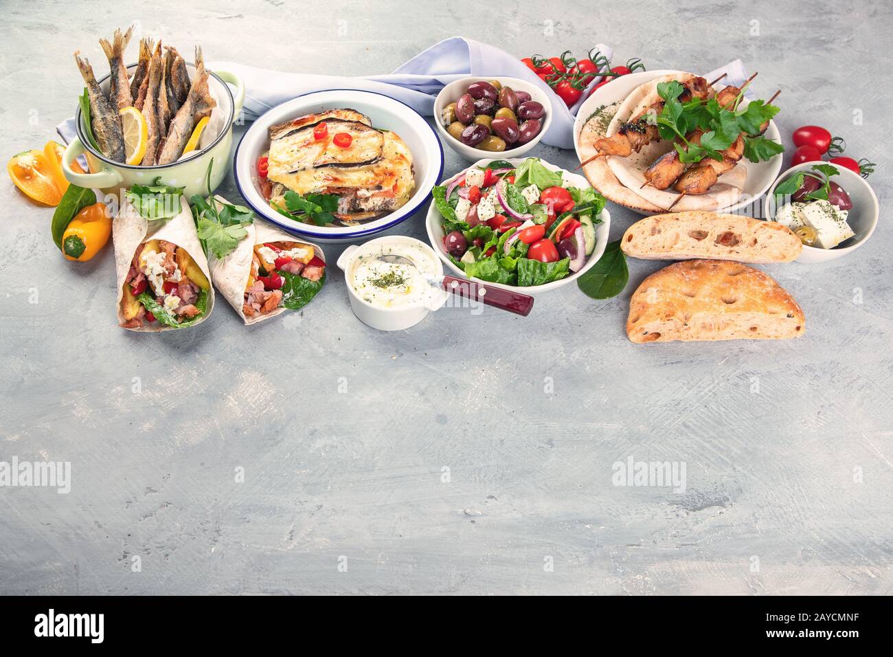 Cibo greco su sfondo grigio. Moussaka, gyros, souvlaki, pita, insalata, olive e verdure. Piatti tradizionali di diversi tipi di piatti greci. Immagine con c Foto Stock