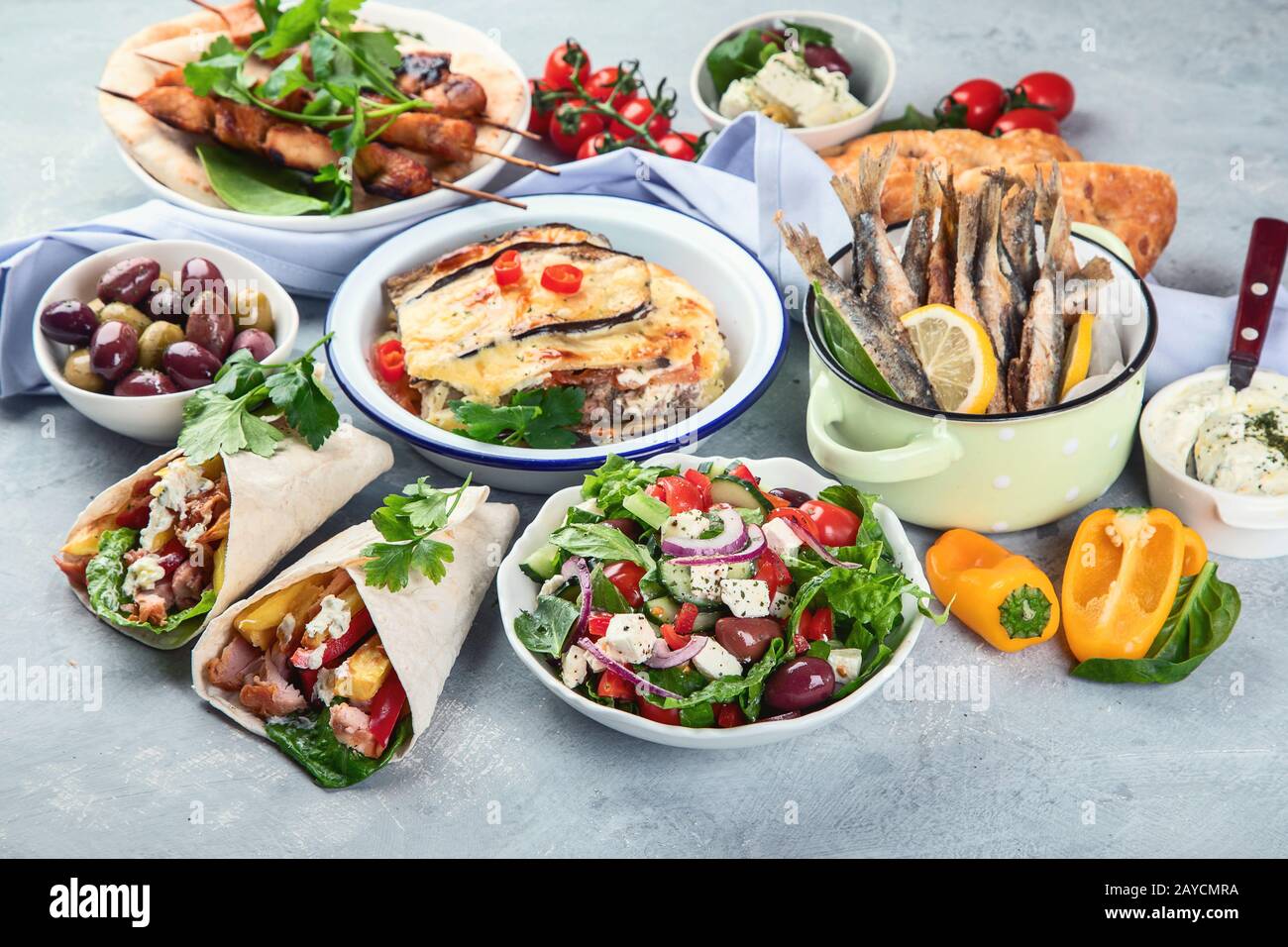 Cibo greco su sfondo grigio. Moussaka, gyros, souvlaki, pita, insalata, olive e verdure. Piatti tradizionali di diversi tipi di piatti greci. Foto Stock