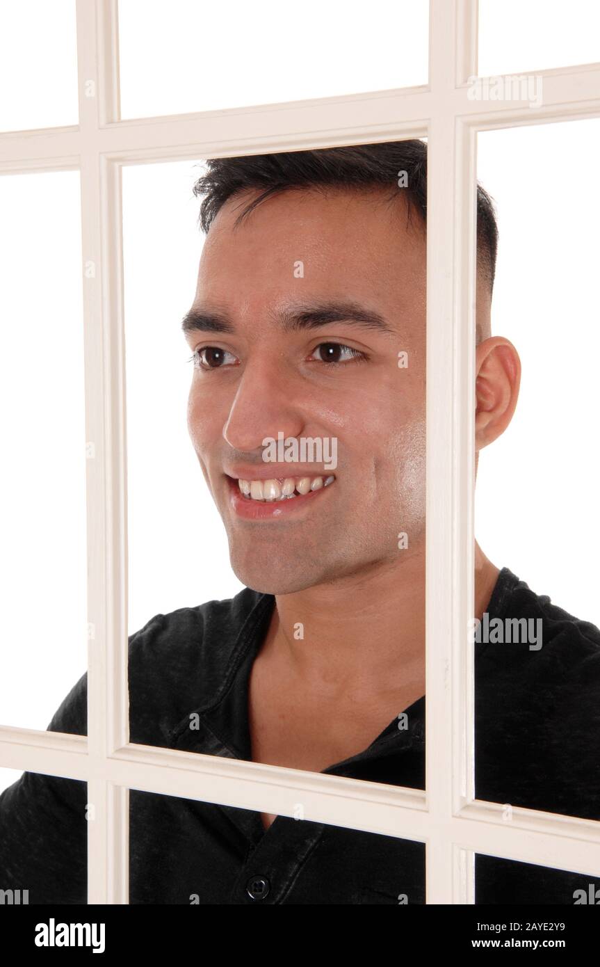 Giovane uomo sorridente dietro una finestra bianca telaio Foto Stock