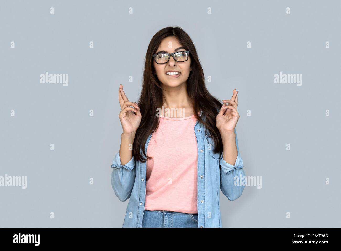 Nervosa ragazza indiana mordente labbra croce dito desiderio di buona fortuna isolato sul grigio Foto Stock