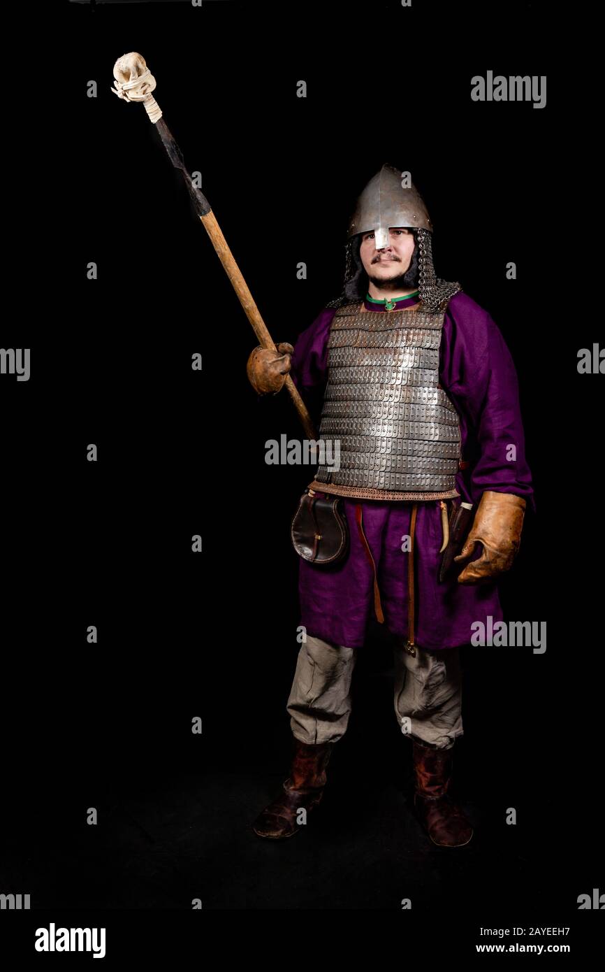 uomo in abito medievale, camicia viola, casco e catena posta tiene una lancia Foto Stock