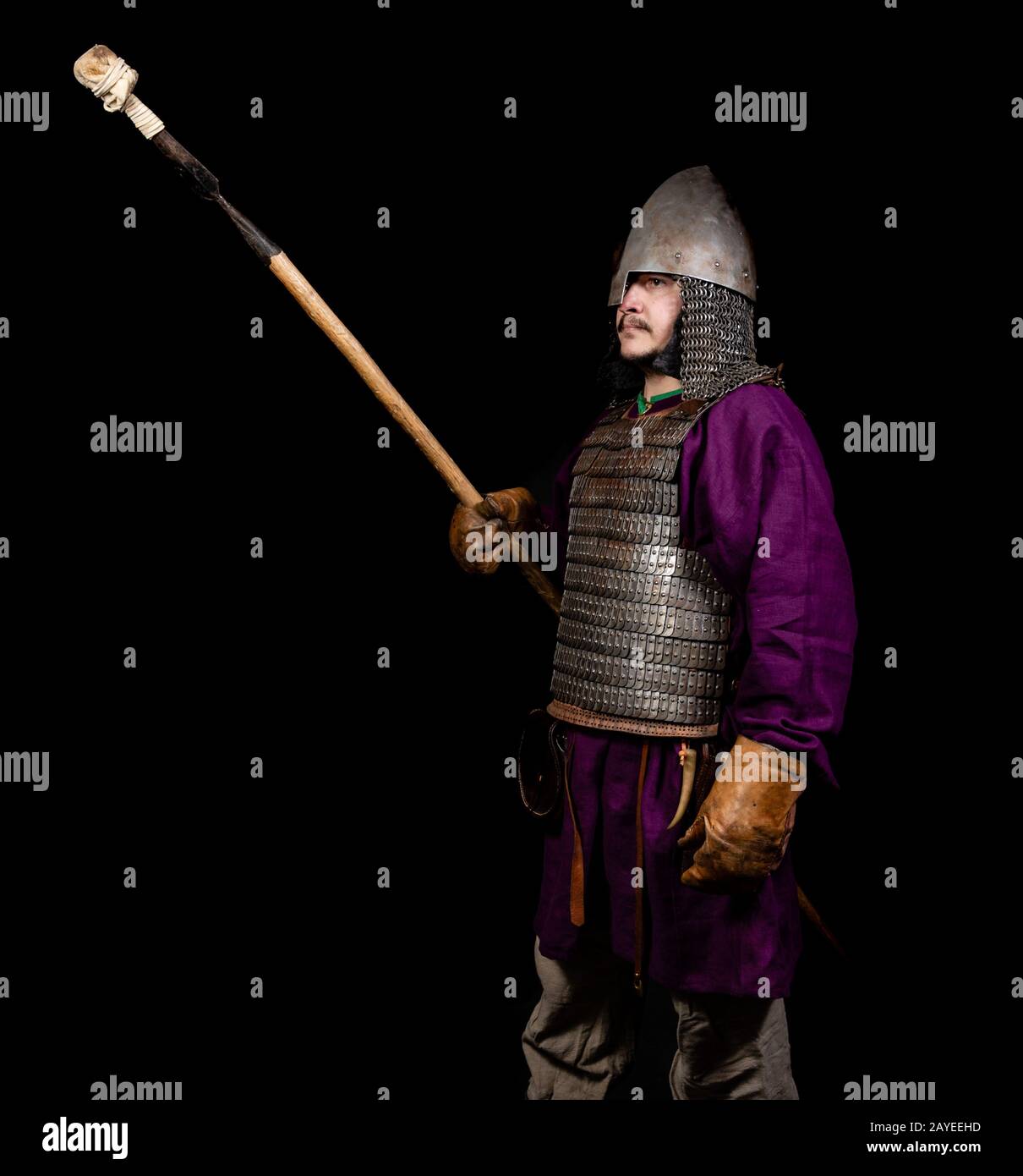 uomo in abito medievale, camicia viola, casco e catena posta tiene una lancia Foto Stock