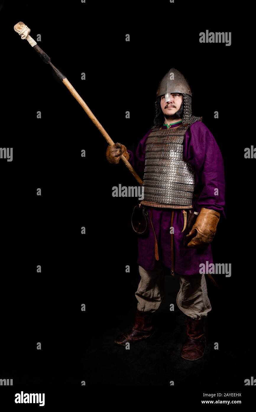 uomo in abito medievale, camicia viola, casco e catena posta tiene una lancia Foto Stock