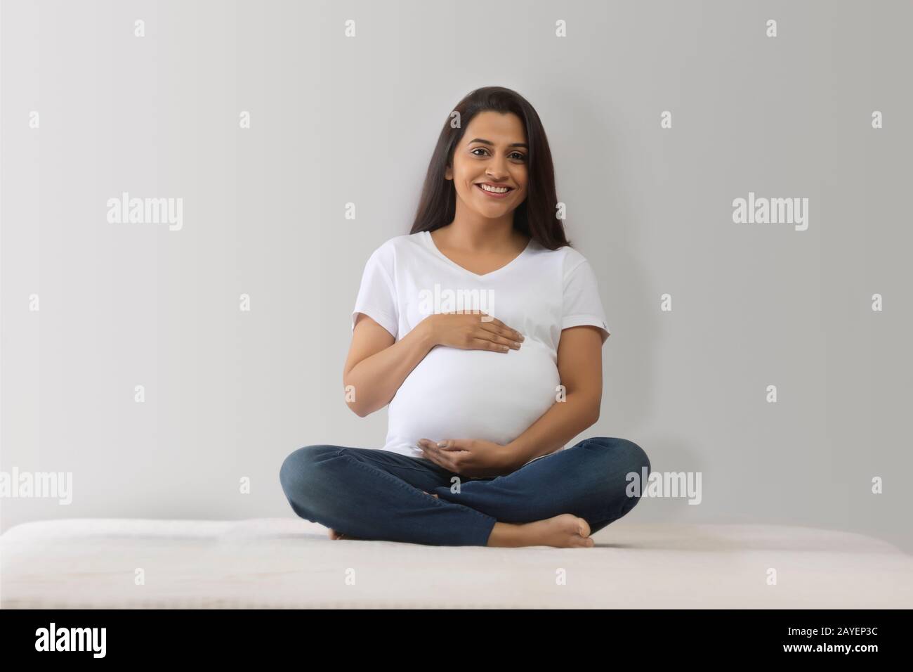 Donna incinta seduta sul letto e tenendo il suo bump bambino. Foto Stock