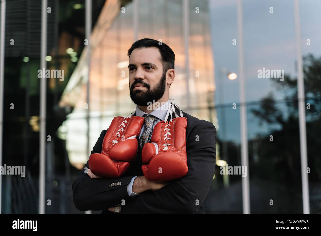 Uomo d'affari con guanti da boxe rossi appesi al collo con le braccia incrociate davanti a un edificio Foto Stock