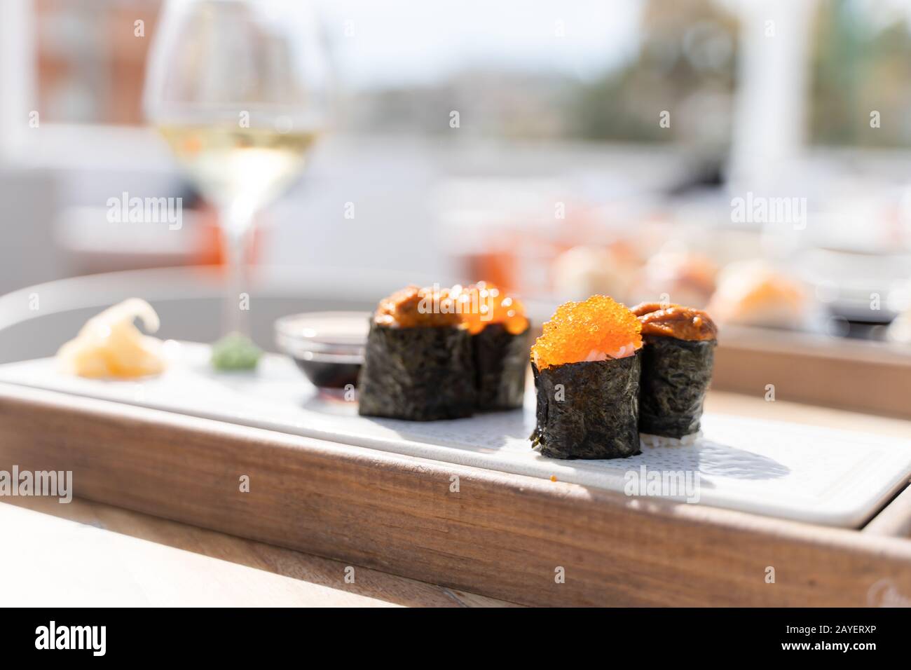 Sushi cibo di uova di pesce servito su un legno piccole tavole con salsa di soia in un ristorante con un bicchiere di vino bianco t egli tabella Foto Stock