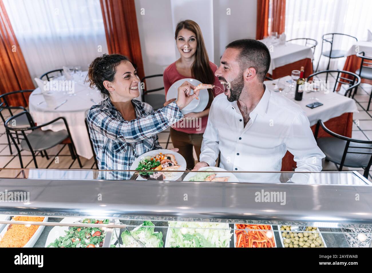 Foto di scorta di una ragazza che gioca l'alimentazione di un gamberetto ad un ragazzo in un ristorante self-service Foto Stock