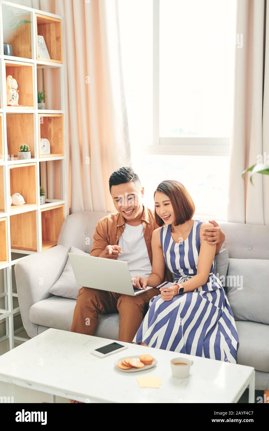 Giovane coppia asiatica che acquista on-line o paga le fatture con carta di credito con il laptop a casa Foto Stock