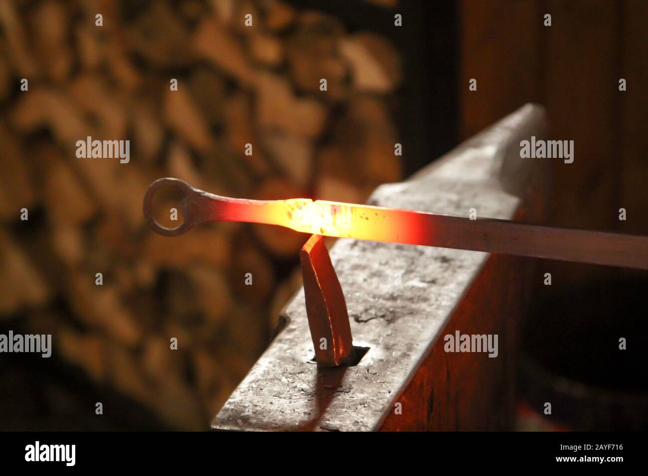 Un fabbro utilizza un martello per lavorare un pezzo di metallo incandescente sull'incudine Foto Stock