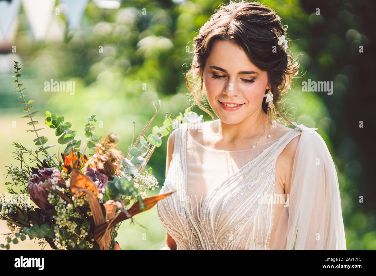 Bella sposa con fiori di bouquet si erge sullo sfondo della foresta. Stile rustico. Bellissima sposa in abiti delicati all'aperto. Clos Foto Stock