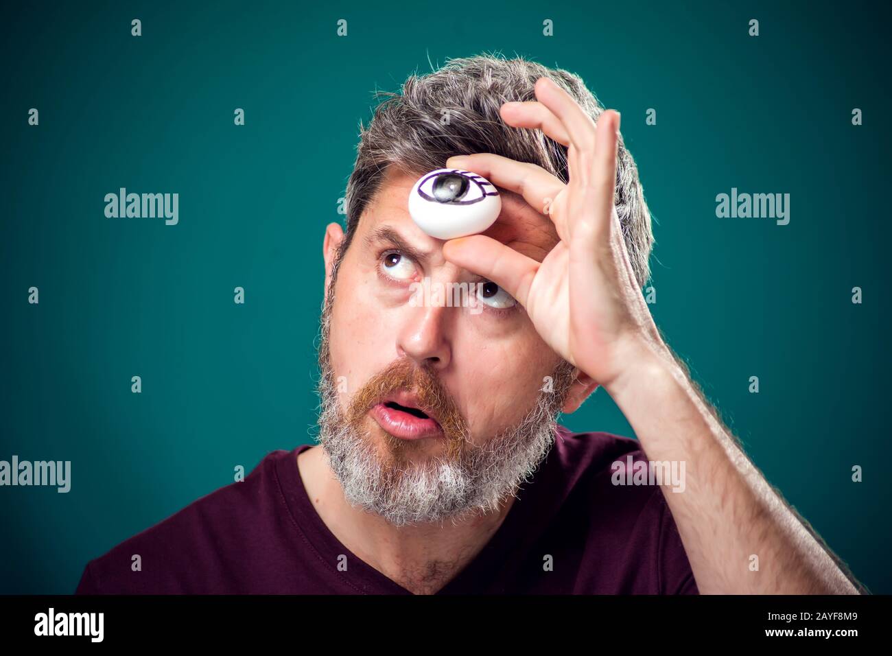 Un ritratto dell'uomo con bearded in t-shirt rossa che tiene l'uovo con l'occhio di disegno dietro forefad come terzo simbolo dell'occhio. Foto Stock