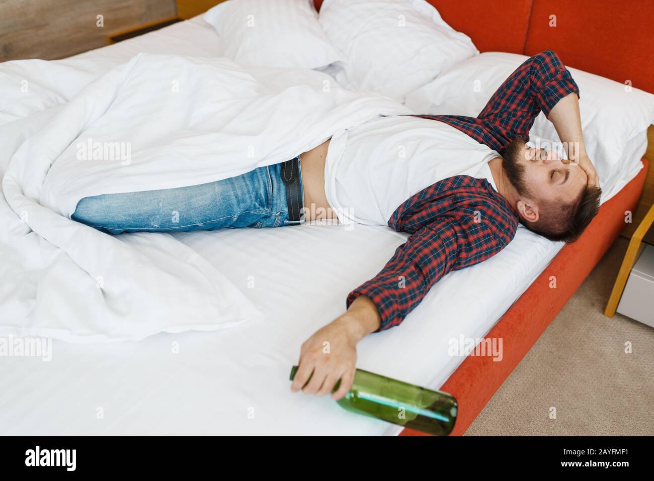 L'uomo ubriaco dorme nel letto con una bottiglia di vino Foto Stock