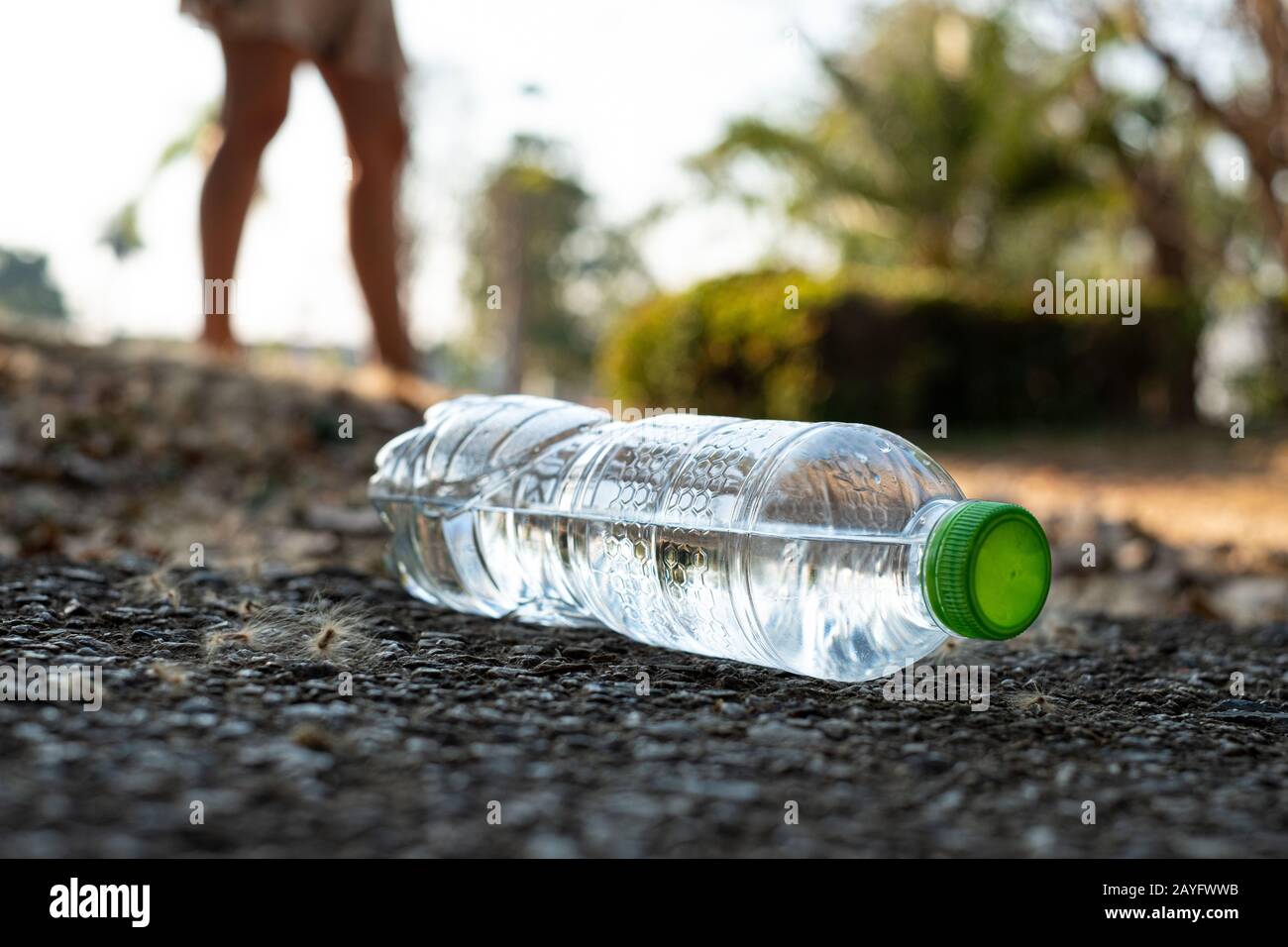 Chiudete la bottiglia di acqua in plastica trasparente con un tappo verde sulla strada nel parco su sfondo sfocato, cestino che viene lasciato fuori dal bidone, cucciolata Foto Stock