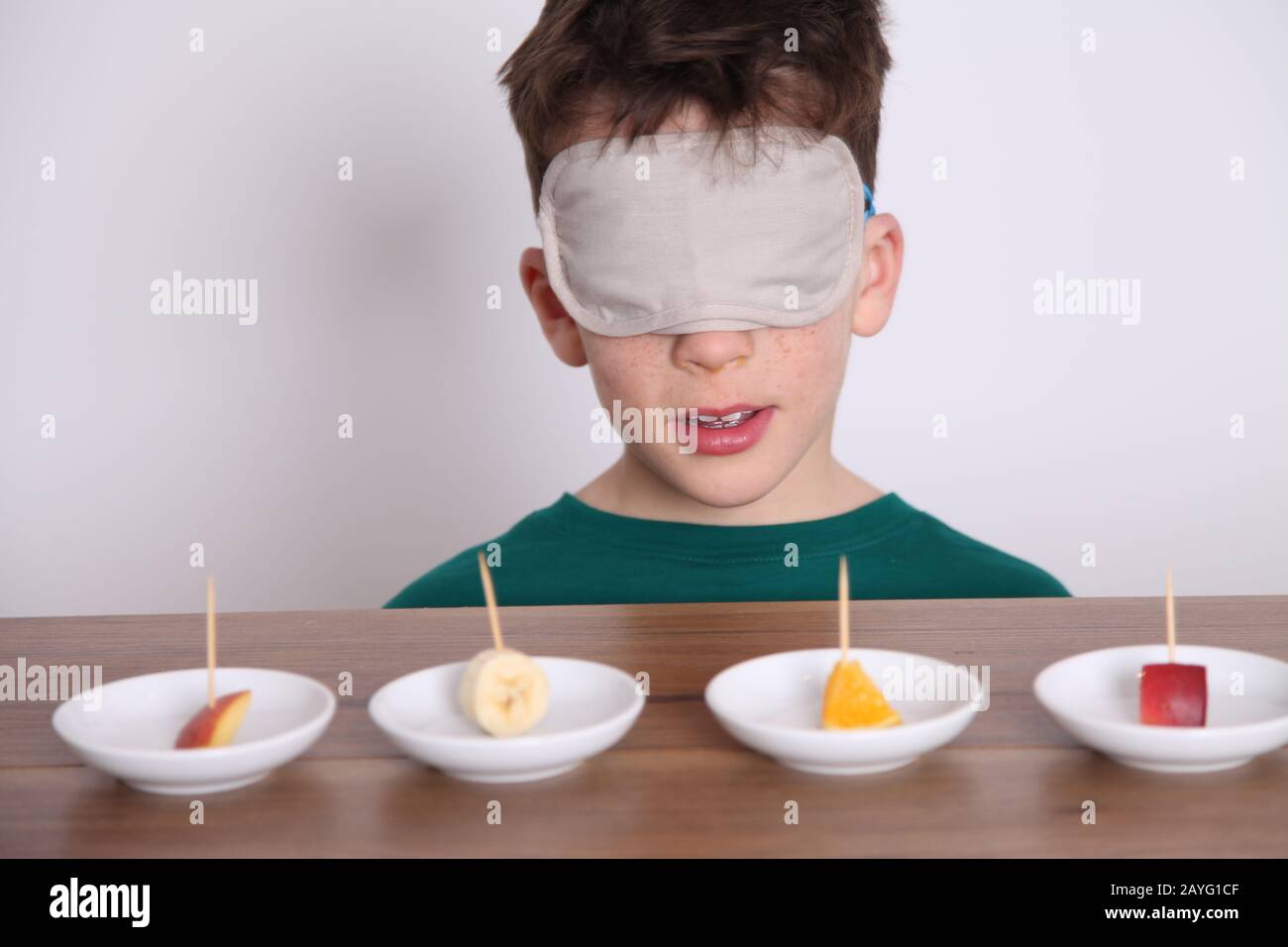 Un ragazzo dai capelli scuri di 8yrs vecchio prende parte ad una prova del gusto ciecfold, assaggio della selezione dei pezzi di frutta ciechi, pesca, banana, arancio, nettarine Foto Stock