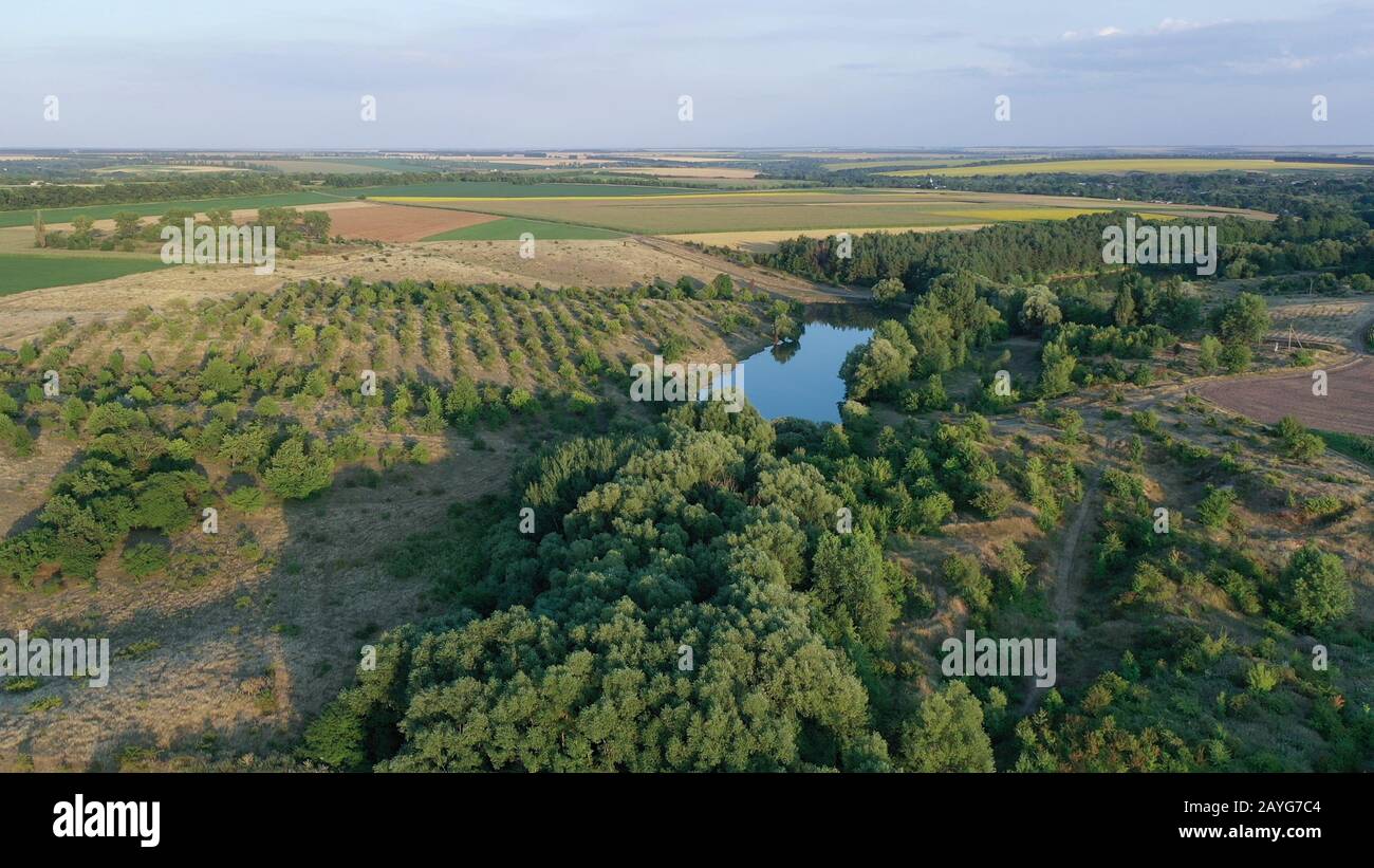 Verde valle e stagno con acqua, giardino e campi con raccolti in serata con luce solare bassa e ombre rugose. Foto Stock