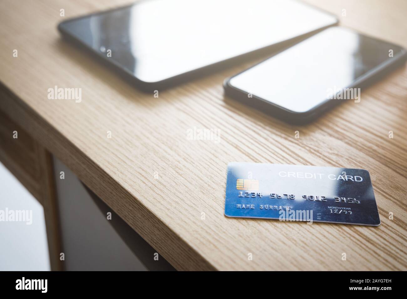 Carta di credito blu con smartphone e tablet su tavolo in legno vicino alla finestra. Foto Stock