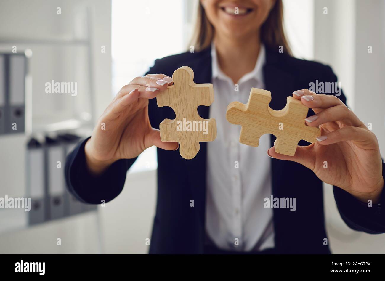 Mani senza volto di una donna d'affari con puzzle in legno in mani in ufficio. Foto Stock