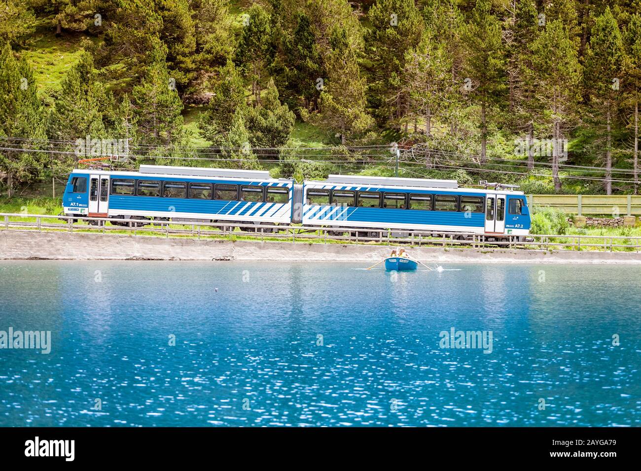 25 LUGLIO 2018, NURIA, SPAGNA: Treno che passa attraverso la valle Nuria contro il primo piano del lago di montagna blu, Spagna Pirenei Foto Stock