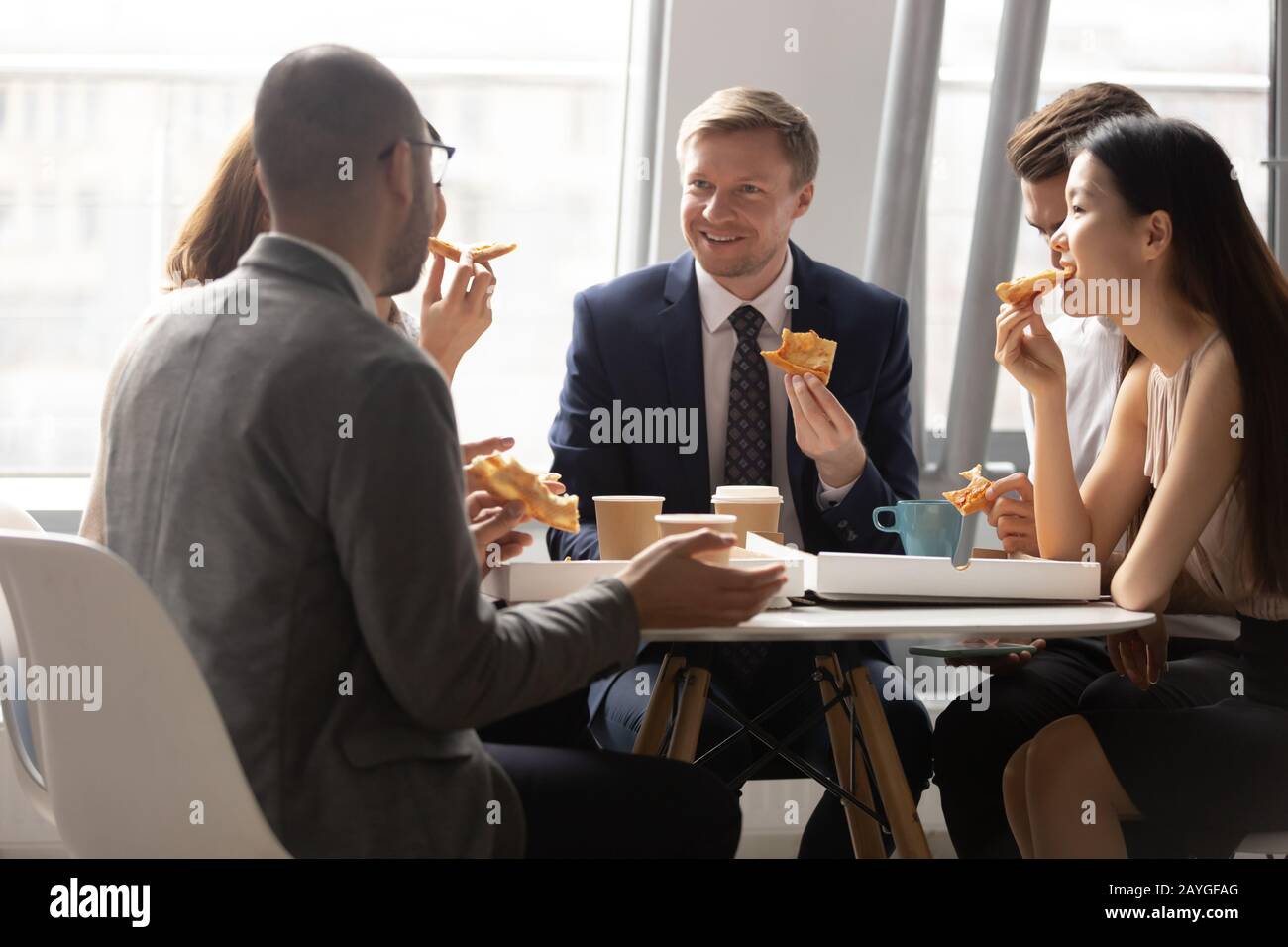 I colleghi multietnici parlano di pizza e caffè durante la pausa pranzo Foto Stock