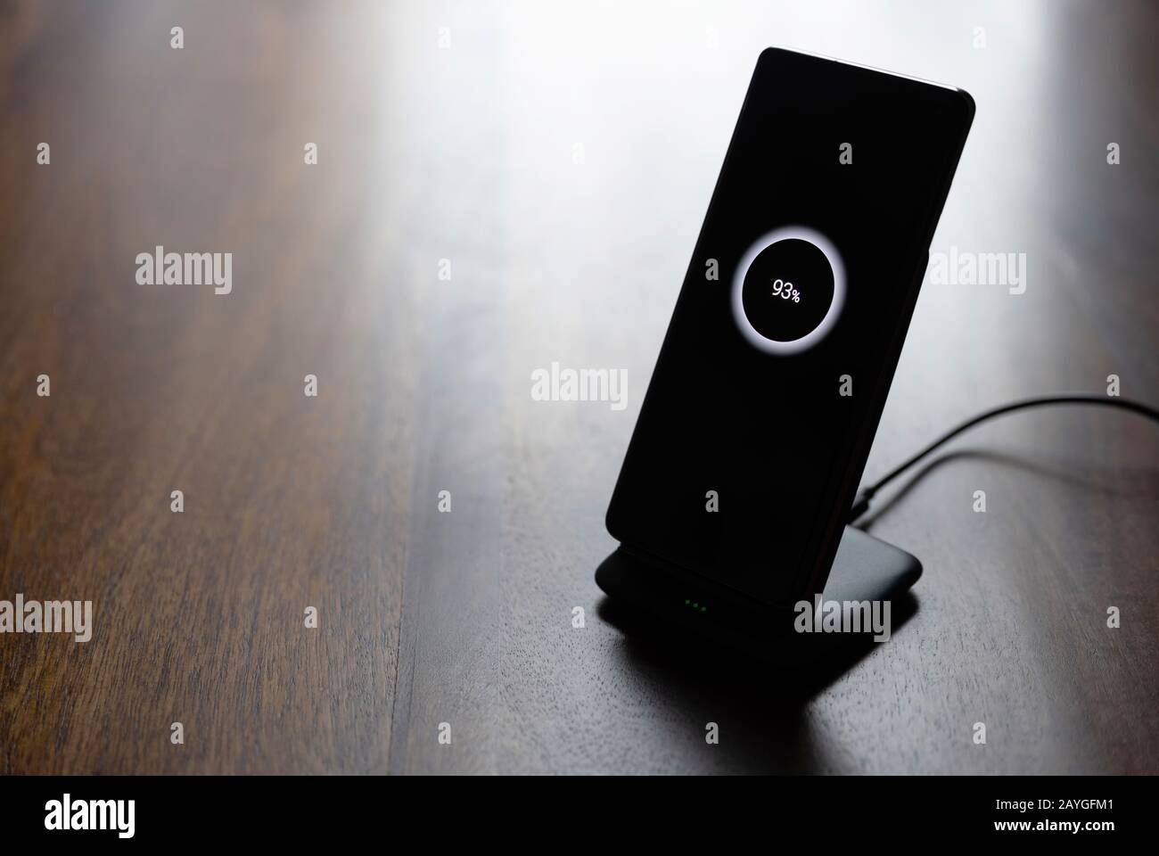 ricarica wireless dello smartphone sul supporto di ricarica con icona del 93% sullo schermo del tavolo in legno Foto Stock