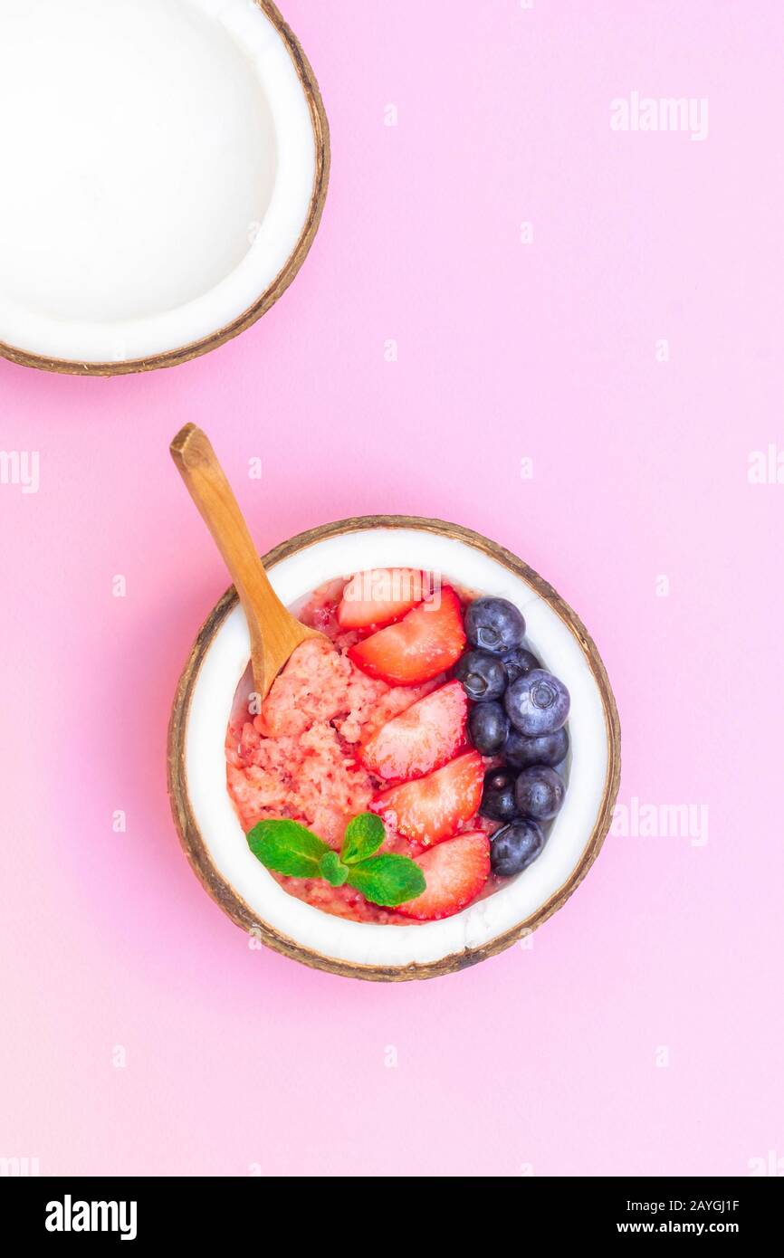 Vista dall'alto della ciotola di cocco con frullati di frutti di bosco sani su sfondo rosa Foto Stock