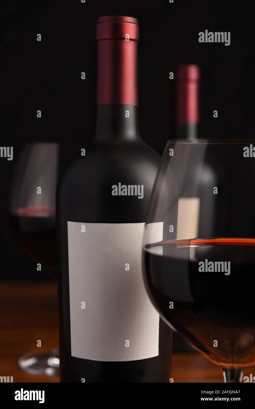 Primo piano e sfondo di una bottiglia di vino rosso con etichetta vuota e bicchieri da vino fuori fuoco. Foto Stock