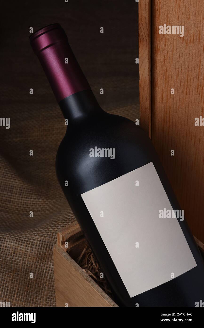 Primo piano di una bottiglia di vino rosso in una scatola di legno. Il flacone ha un'etichetta vuota Foto Stock