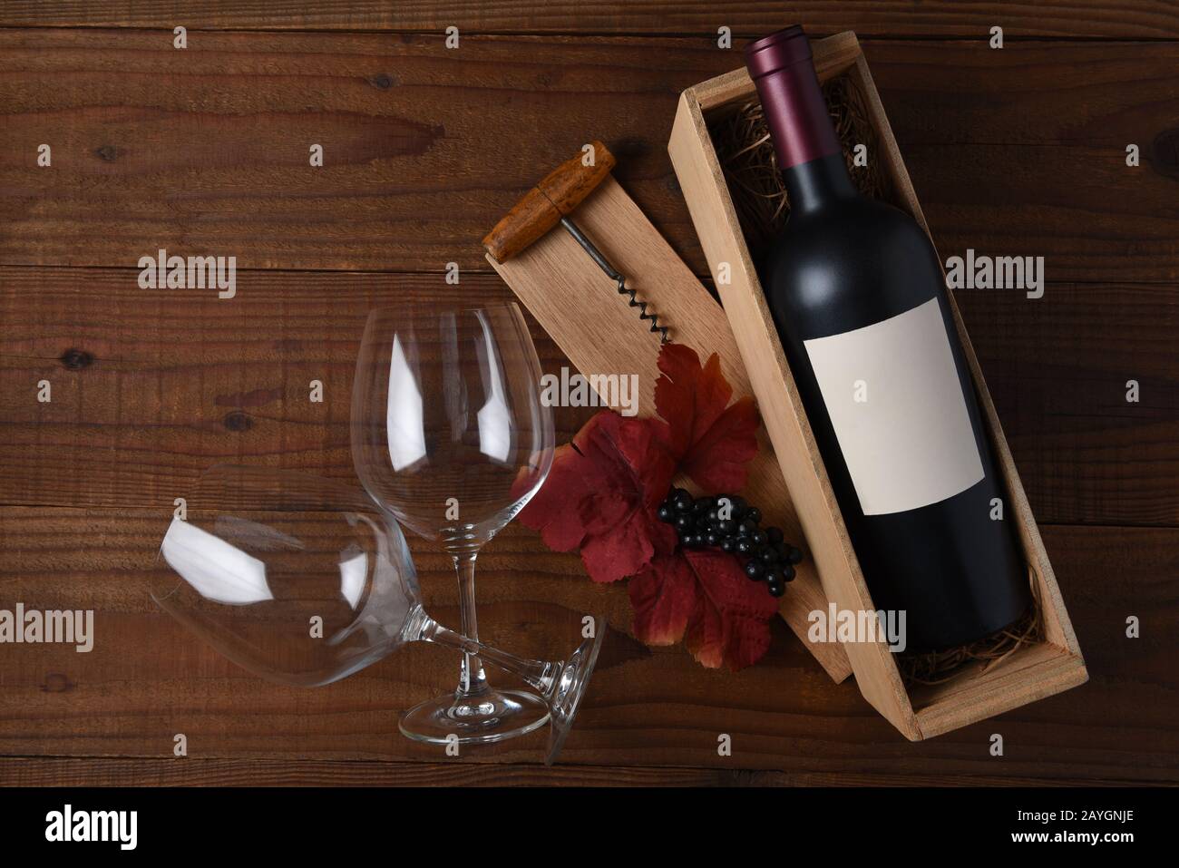 Vino ancora vita una bottiglia di vino con etichetta in bianco in una scatola di legno con due bicchieri, cavatappi, foglie e uva. Piatto Con spazio copia su rustico da Foto Stock