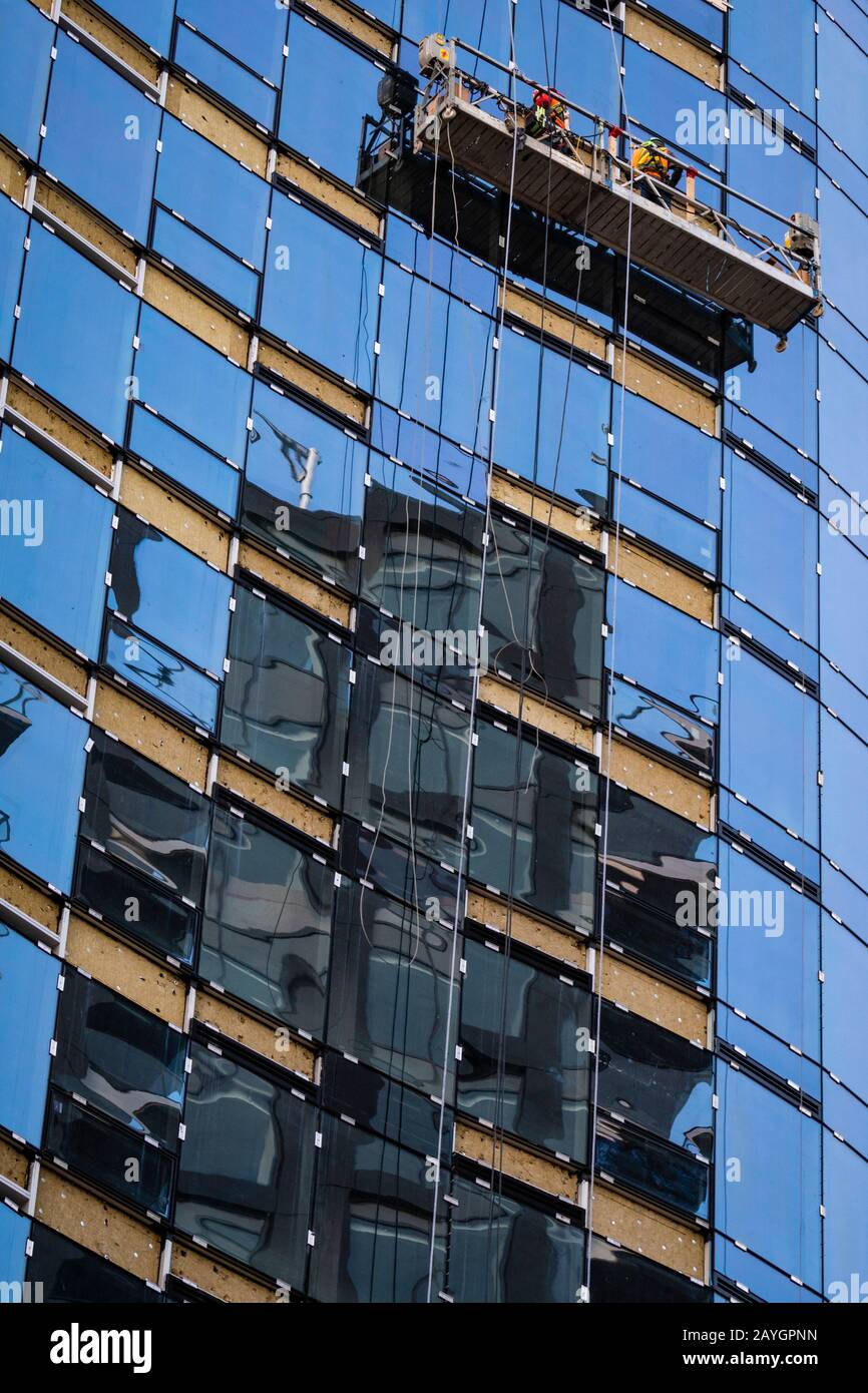 Lavoratori ad un'altezza che pende dal lato di un alto edificio di vetro su un palcoscenico di oscillazione. Foto Stock