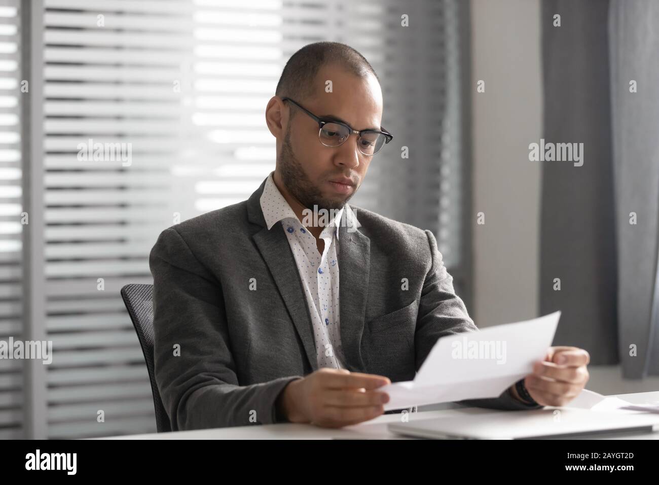 Un dipendente di sesso maschile concentrato che legge la lettera cartacea sul posto di lavoro Foto Stock