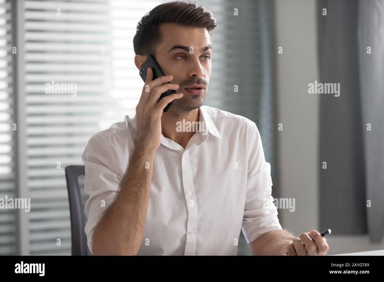 Uomo d'affari millennial parla su client di consulenza cellulare in ufficio Foto Stock