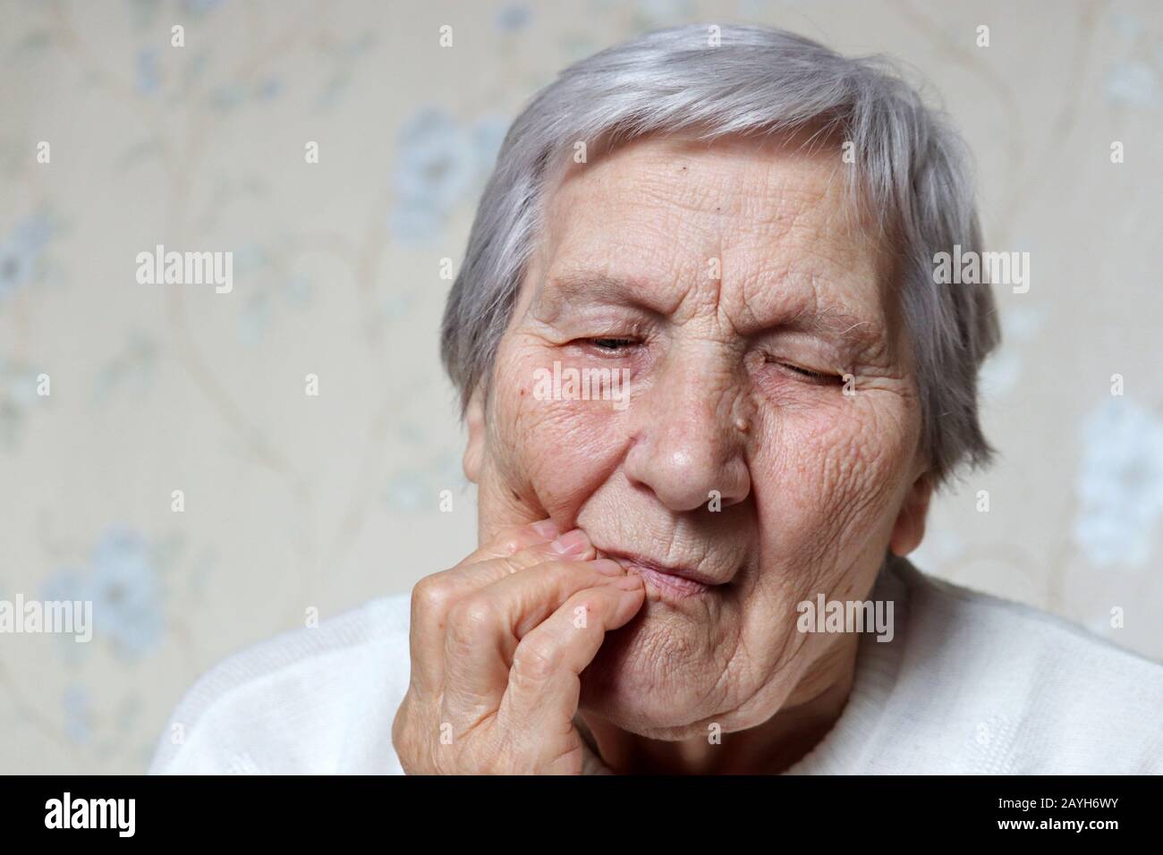Donna anziana che tiene la guancia, femmina con capelli grigi che soffrono di un mal di denti. Concetto di dolore ai denti, malattia delle gengive e vecchiaia Foto Stock