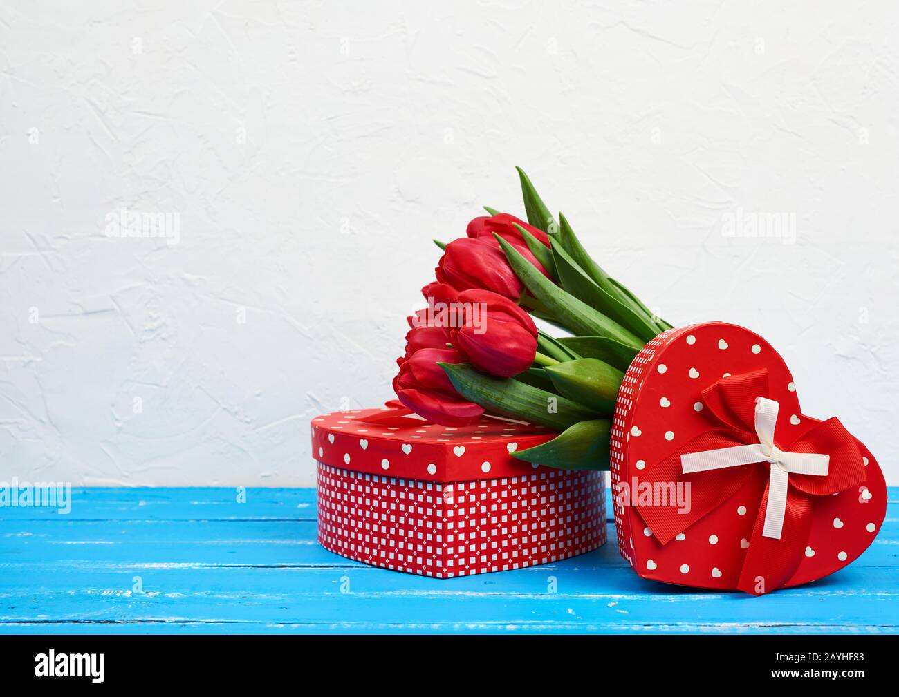 bouquet di tulipani rossi in fiore con foglie verdi, regali avvolti su uno sfondo di legno blu. Sfondo festivo per compleanno, San Valentino, anniversaria Foto Stock