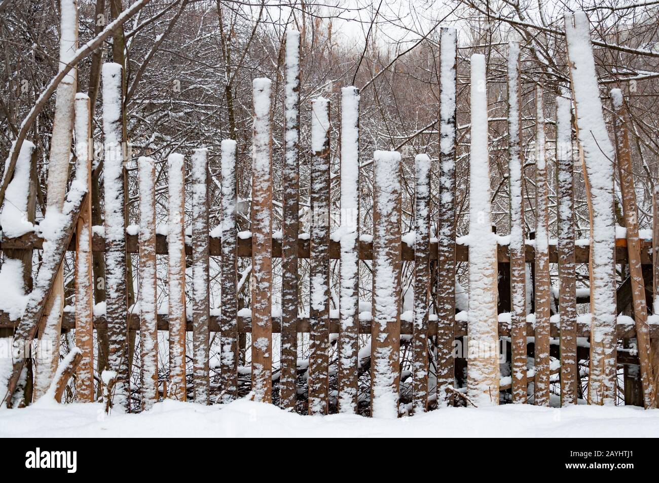 Una vecchia recinzione in legno fatta di tavole di diverse altezze coperte di neve. Dietro il recinto c'è una profonda gola innevata sovracresciuta con la foresta Foto Stock