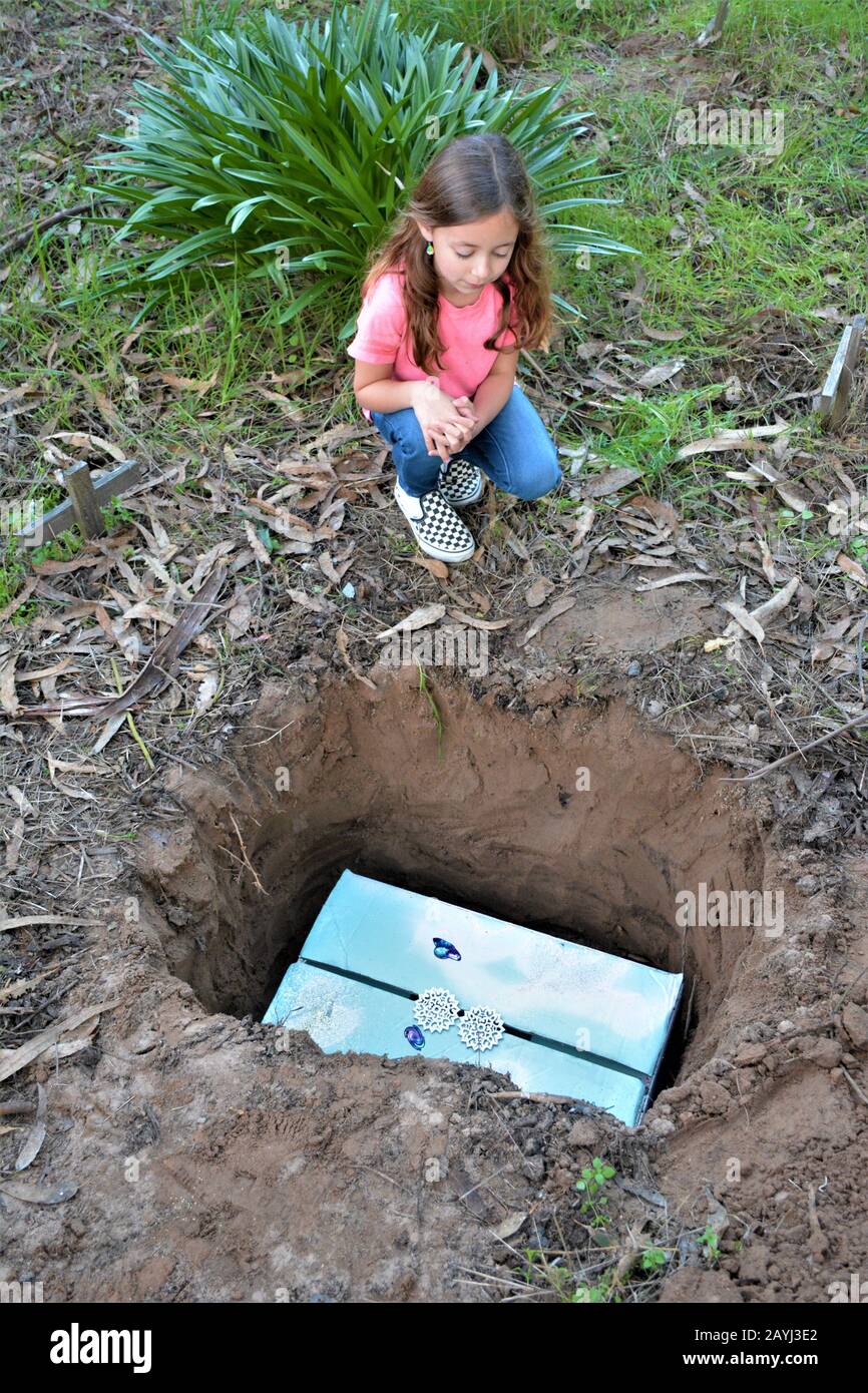 Una vera e propria bambina di 7 anni triste guardando la tomba del suo cane da compagnia morto che è morto e sepolto nel cortile della casa di famiglia in California Foto Stock